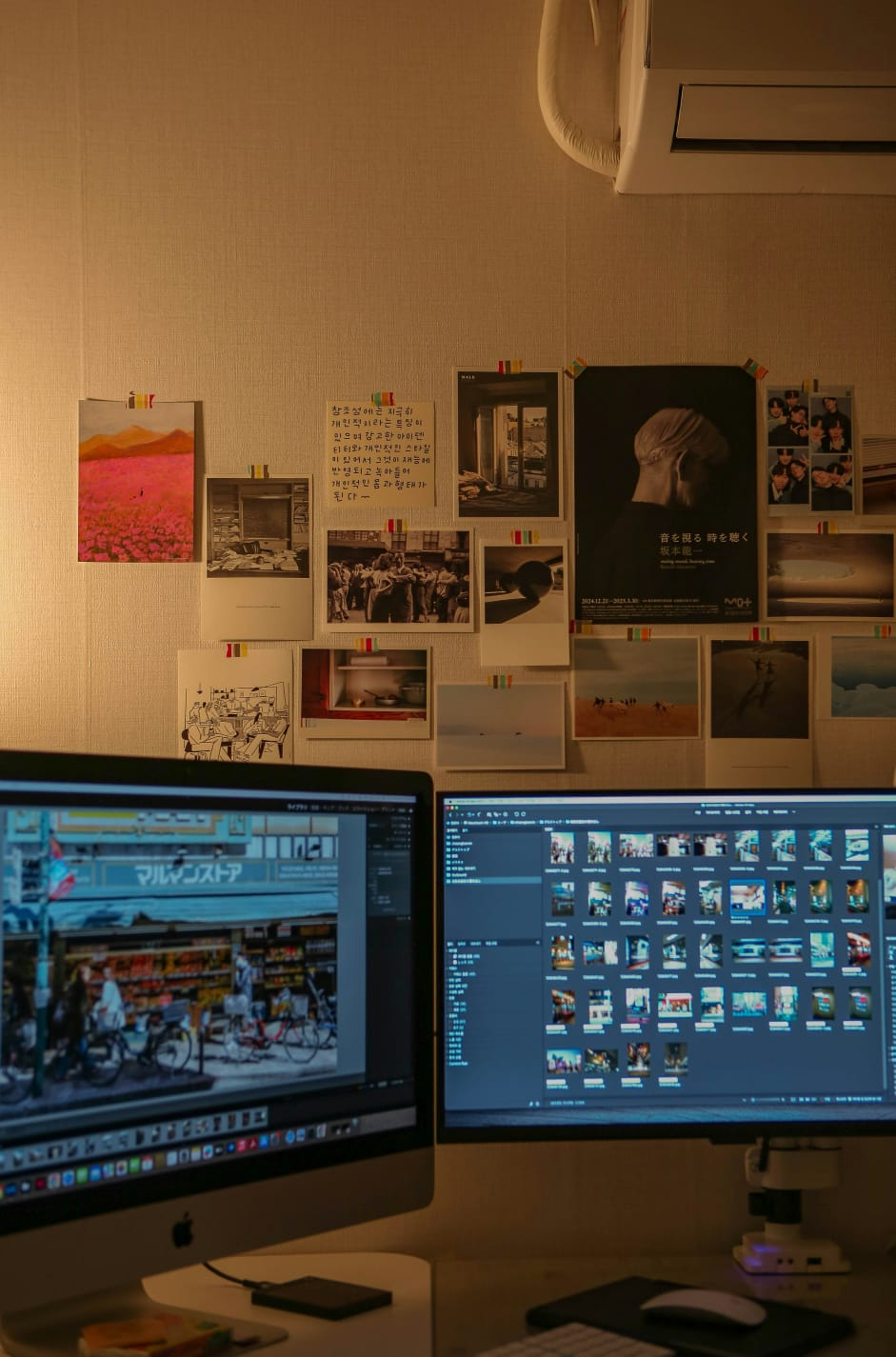 Creative design studio workspace with dual monitors showing design software and inspiration wall with various posters and creative materials